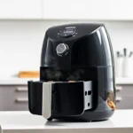 A sleek black CHEFMAN 2 Qt Mini Air Fryer compact air fryer on a modern kitchen counter, with steam rising from the basket, professional product photography, clean white background available